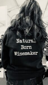 Woman with her back to the camera with a shirt that reads "Natural Born Winemaker"